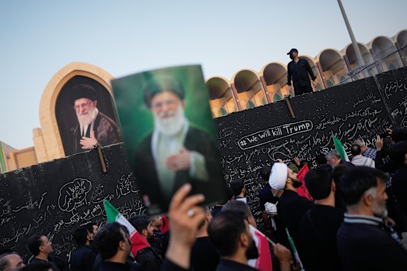 A mourner carries a portrait of Khamenei past a wall bearing the message “We Will Kill Trump” in Tehran. 
