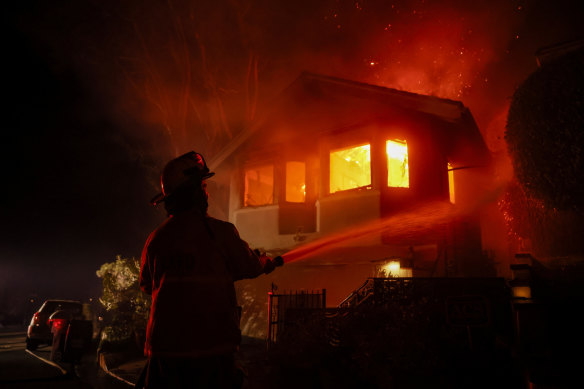 A firefighter works as the Palisades fire burns a house in the hill next to the Getty Villa on Wednesday. 