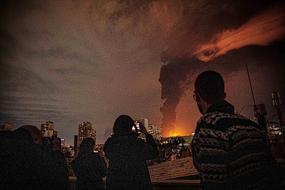 Residents of Tehran look on as flames and smoke rise from an oil storage facility struck by Israeli troops.