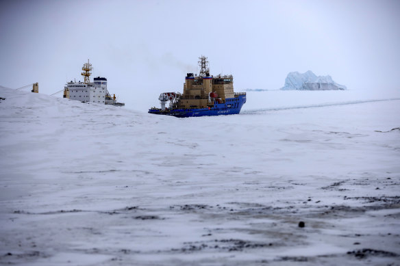 An Icebreaker makes the path for a cargo ship with an iceberg in the background near a port on the Alexandra Land island near Nagurskoye, Russia, Monday, May 17, 2021.