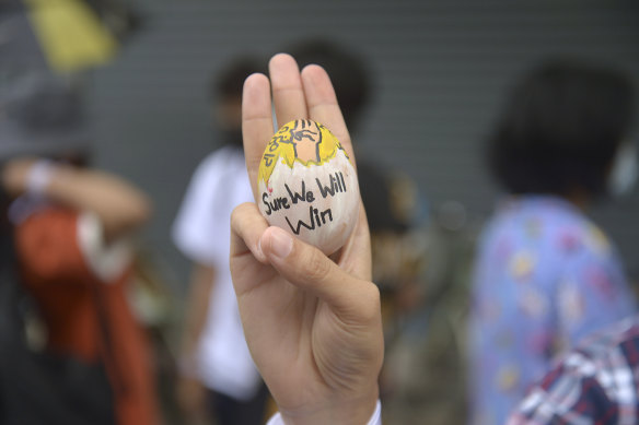 Anti-coup protester raises a decorated Easter egg along with the three-fingered symbol of resistance during a protest against the military coup on Easter Sunday.