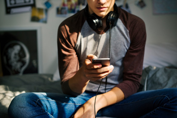 A teen sits in his bedroom and stares at his phone.