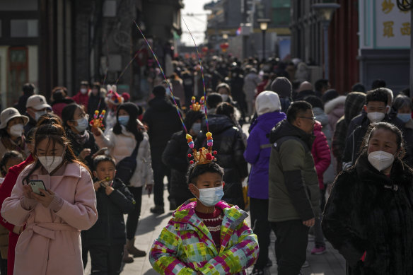Yüz maskesi takan bir çocuk, Pekin'deki Yeni Ay Yılı tatilinin ilk gününde ziyaretçilerle dolup taşan Qianmen'de bir yaya alışveriş caddesinde tur atıyor