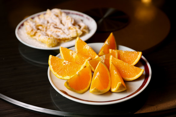 Dessert platter of orange wedges and icing-sugared pastries.