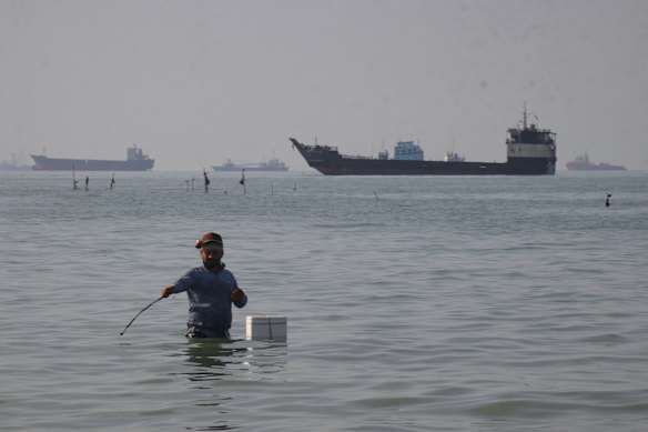 A man apparently fishes as bulk carriers, cargo ships, and service vessels line the horizon in the Strait of Hormuz off Bandar Abbas, Iran.