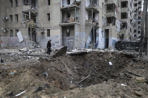 A local resident passes by a crater caused by a Russian rocket attack, which hit several buildings in central Kharkiv.