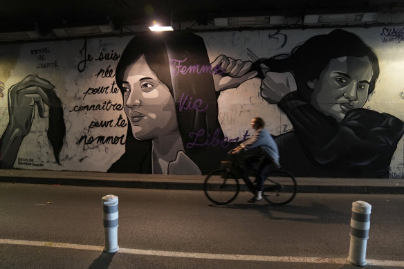 A woman rides bicycle front of a mural depicting women cutting their hair to show support for Iranian protesters.