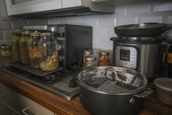 Jars of fermenting fruits and vegetables, left, sit on top of a retired gas stove replaced by an electric cooker, right, in Josh Spodek’s kitchen.