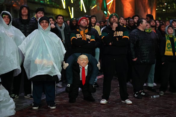 Fans at Fed Square, including a man in a costume that made it look as if he was on Donald Trump’s shoulders, watch the first half.