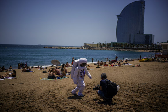 A man films a person dressed as an astronaut on the beach of Barcelona, Spain, where tourist growth has been matched by growing COVID infections.
