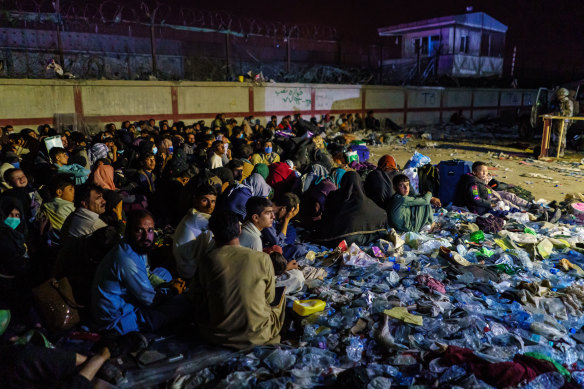 Afghan refugees crouch in a group as British military secure the perimeter outside the Baron Hotel, near the Abbey Gate, in Kabul, Afghanistan.