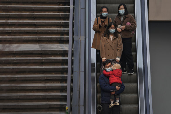 People wearing face masks to protect from COVID-19 take an escalator at a commercial office building in Beijing, on Sunday, November 28.