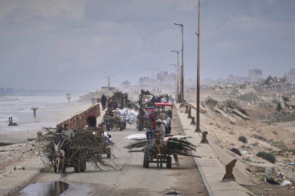 Displaced Palestinians, carrying their belongings, wood and other items, move between southern and northern Gaza along a beach road on Friday.
