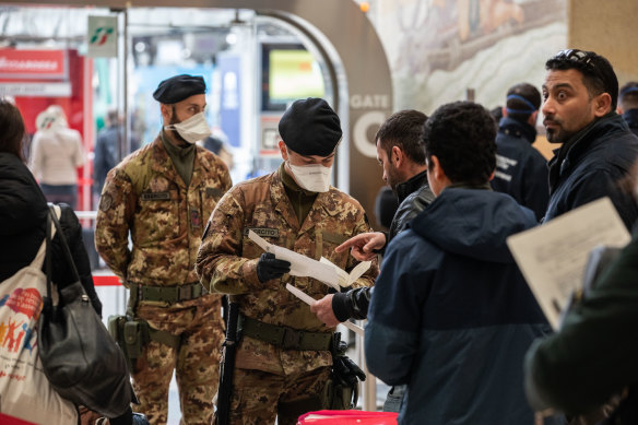 Italian police process passengers leaving from a train station in Milan.