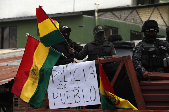 Police against the re-election of President Evo Morales stand on the rooftop of a police station just meters away from the presidential palace waving national flags, near a sign that reads in Spanish: "The police is with the people".