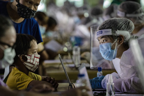 A medical worker interviews a child queuing for a free COVID-19 swab in Manila. 