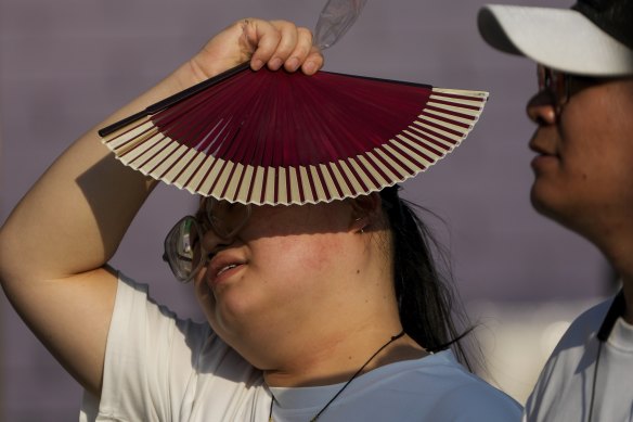 A woman uses a fan as she walks on a hot day in Beijing.