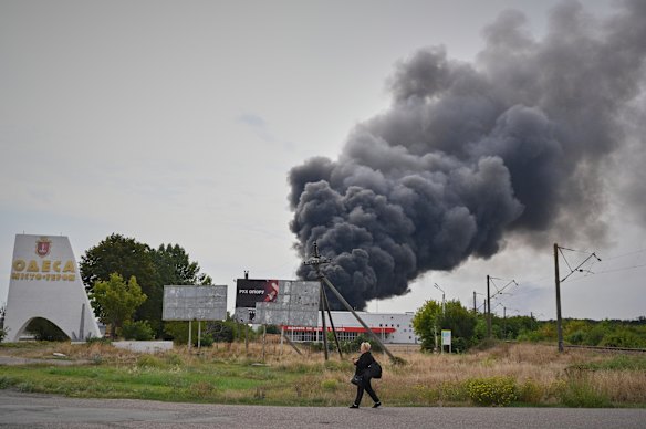 A woman walks past a burning warehouse in Odesa, struck by a Russian drone.