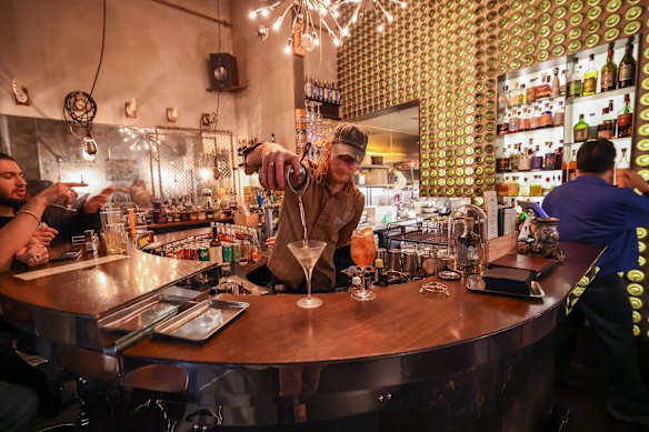 The back bar (right), on a backlit wall made of wine bottle bases, is stocked with several of Bar Ampere’s own concoctions.