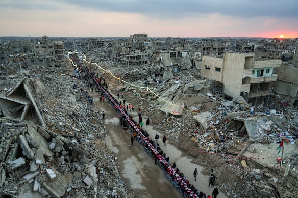 As the sun sets, Palestinians sit at a large table surrounded by the rubble of destroyed homes and buildings as they gather for iftar, the fast-breaking meal, on the first day of Ramadan in Rafah, southern Gaza Strip on Saturday.
