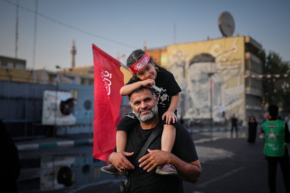 A man carries a child holding a Shiite religious flag outside the Imam Khomeini Mosalla Grand Mosque in Tehran during one of the funeral ceremonies for the slain Iranian political and religious leader.