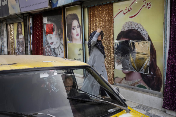  A woman walks past beauty salons with window decorations which have been defaced in Kabul.