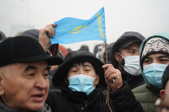 Demonstrators, one of which holds a national flag, gather near a police line during a protest in Almaty, Kazakhstan. Demonstrations started after the government raised the price of fuel at the weekend.