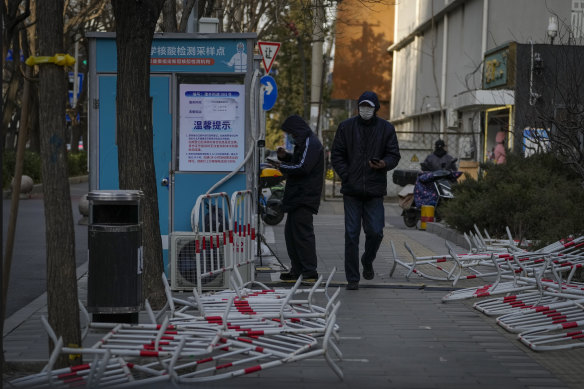 A man walks by a resident registering to get his COVID-19 throat swab near discarded barricades around a coronavirus testing site in Beijing on Wednesday.