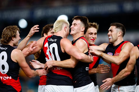 Essendon players celebrate blond forward Nate Caddy’s goal.