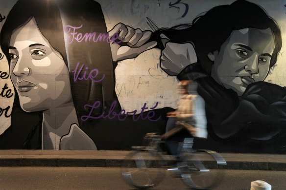 A man rides bicycle front of a mural depicting women cutting their hair to show support for Iranian protesters standing up to their leadership over the death of a young woman in police custody, in a tunnel in Paris, France.