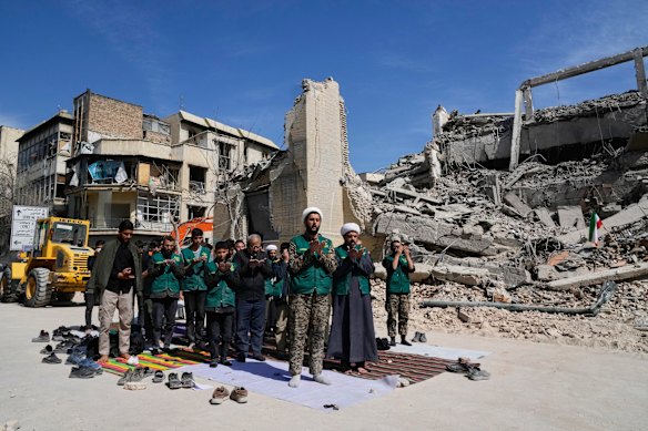 A cleric leads volunteers in prayer next to a police facility struck in Tehran.