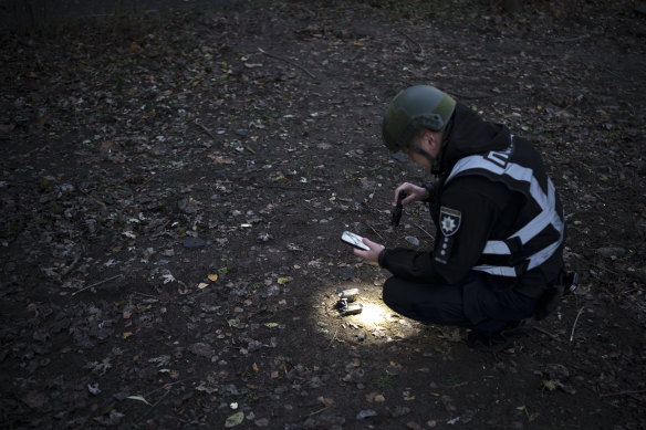 A Ukrainian police officer uses a flashlight to search for drone debris near the site of an explosion following a Russian drone attack in Kyiv.
