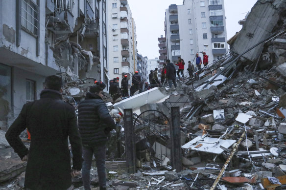 People and rescue teams try to reach trapped residents inside collapsed buildings in Adana, Turkey.