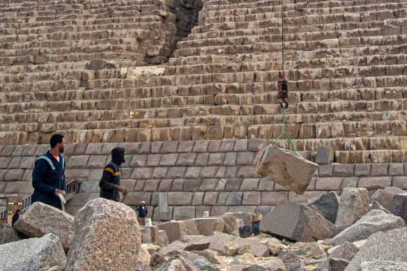 Workers watch as a stone is lifted by a crane during a conservation project by the base of the Pyramid of Menkaure.