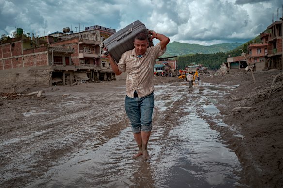 A Nepalese resident carries belongings across a road heavily covered in mud.