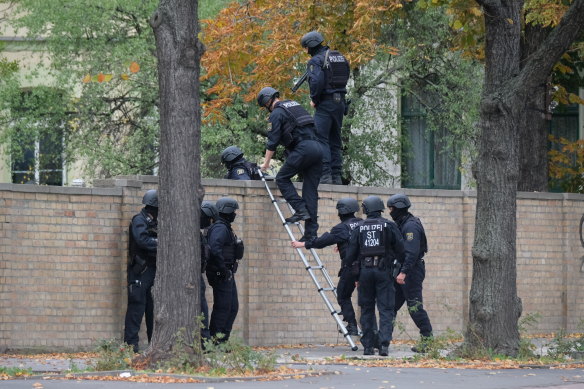 Police officers climb over a wall at the crime scene in Halle, Germany.