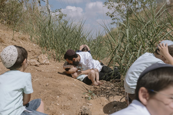 Israelis take cover as a siren sounds a warning of incoming rockets fired from the Gaza Strip in Rehovot, Israel.