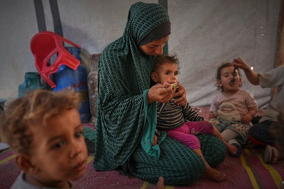A mulher palestina alimenta os meninos na barraca para cobrir a família na cidade central de Gaza.