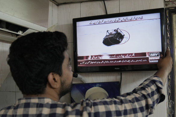 A man watches a news channel airing news regarding people trapped in a cable car, at a barber shop in Lahore.