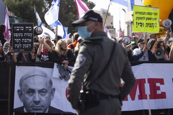 A police officer stands guard in front of protesters as Prime Minister Benjamin Netanyahu’s motorcade arrives at his corruption trial hearing on Monday.