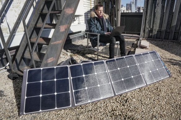 Josh Spodek works on his laptop while it charges on a portable solar kit set up on the rooftop of his Greenwich Village apartment building.