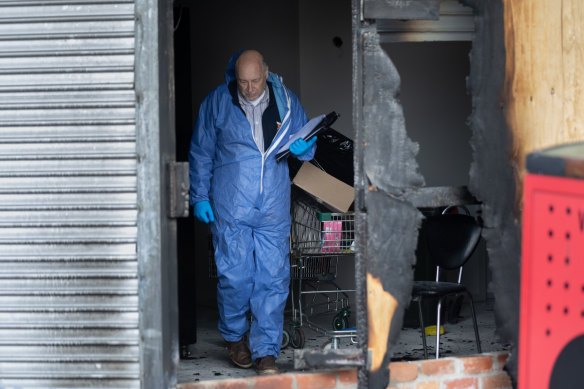 A police officer inspects the burnt shopfront of a Hadfield tobacconist attacked on Wednesday morning.