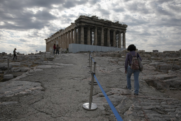 An employee of the Greek Culture Ministry walks alongside a belt separating visitors into sections at the archaeological site of the Acropolis, in Athens.