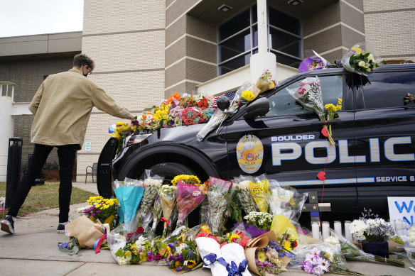 A man leaves a bouquet on a police car parked outside the Boulder Police Department following the shooting. 