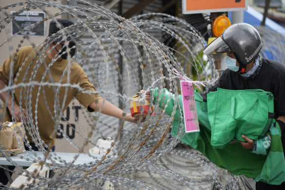 A resident, left, receives food from a delivery man through barbed wire at Segambut Dalam on the outskirts of Kuala Lumpur.