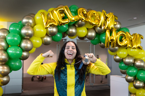 Caitlin Parker shows off her medal as Olympians are welcomed by friends and family as they arrive at Melbourne Airport on Wednesday.