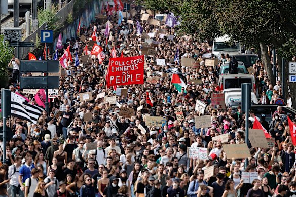 Students with a large red banner reading “Police officers, enemy of the people” march in Rennes.