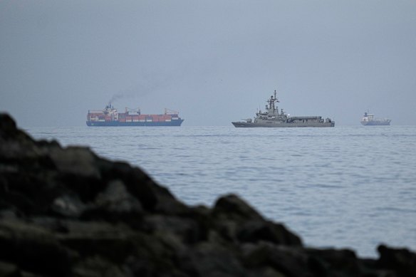 A UAE navy ship sails next to a cargo ship in the Strait of Hormuz. The key waterway remains effectively closed.
