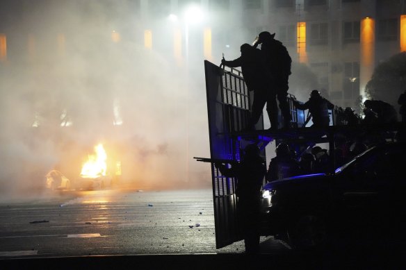 A police car on fire as riot police prepare to stop protesters in the centre of Almaty, Kazakhstan. 