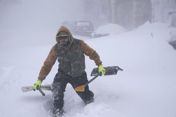 Travis Sanchez trudges over a snowdrift with a pair of shovels for a stranded motorist on Chenango Street in Buffalo, NY.